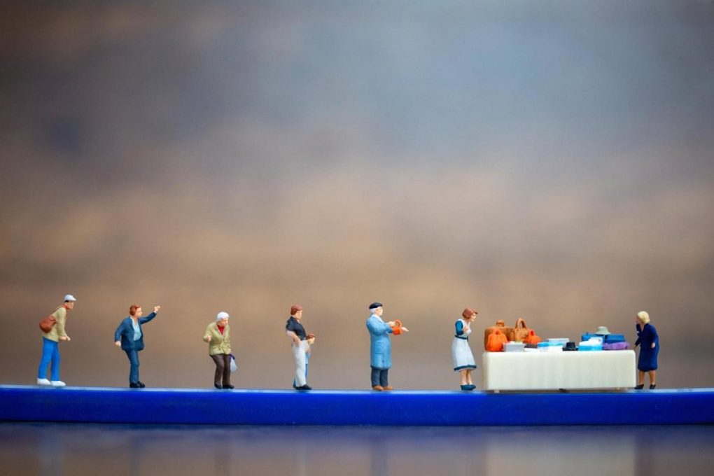 Miniature figures standing in a long queue at a service counter, illustrating traditional queue systems